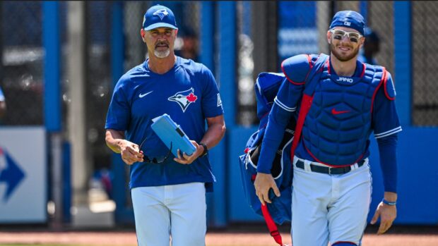 A Toronto Blue Jays coach and player in baseball gear walking outdoors on a sunny day