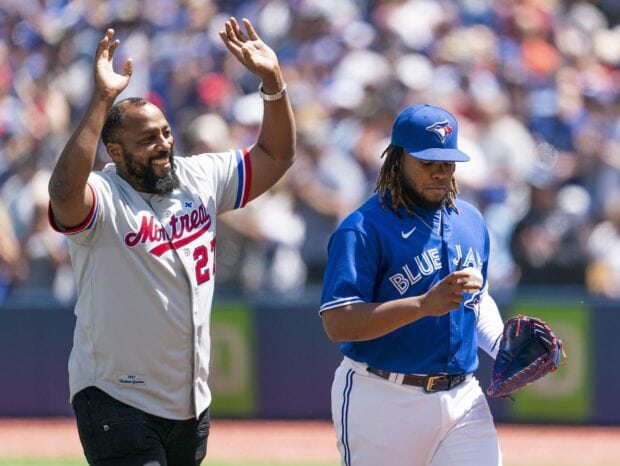 A Toronto Blue Jays player walking on the field alongside a man in a Montreal jersey raising his hands