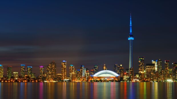 Toronto skyline at night with illuminated buildings and the CN Tower reflecting on the water