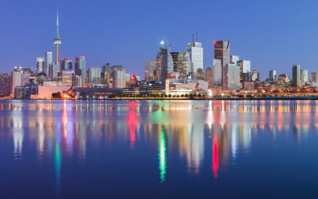 Toronto skyline viewed at dusk with colorful lights reflecting on water