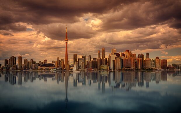Toronto skyline with tall buildings reflecting on calm water under dramatic cloudy sky