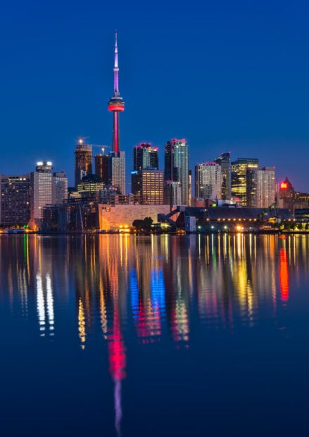 Toronto skyline at dusk with illuminated buildings and CN Tower reflection on water