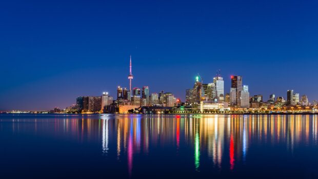 Toronto skyline reflecting on water at night with colorful lights and clear sky