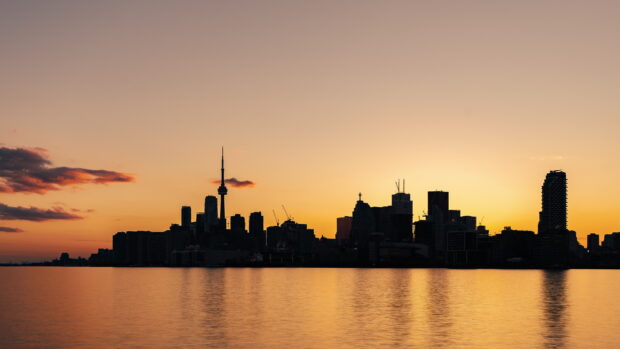 Toronto skyline silhouette against a golden sunset reflecting on the water