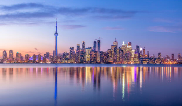 Toronto skyline with illuminated buildings reflected in calm water at dusk