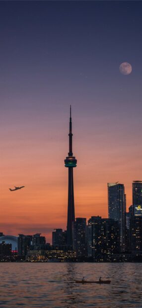 The Toronto skyline features the iconic tower during sunset with water and a boat in the foreground