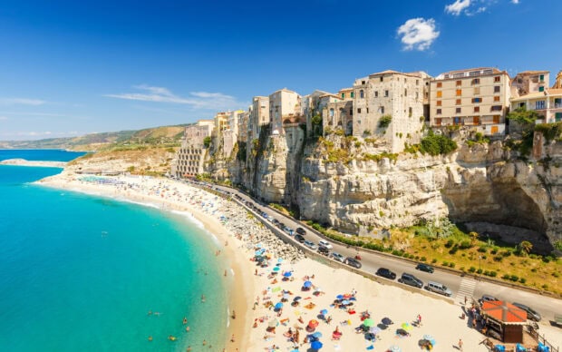 Beautiful Tropea coast with colorful umbrellas and cliffside buildings on a sunny day