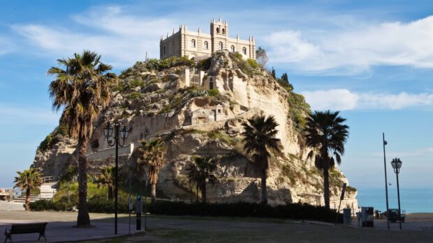 Historic Tropea castle on rocky hill with palm trees under blue sky