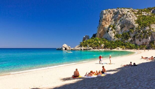 Turquoise sea and rocky cliffs in Tropea with people relaxing on the beach