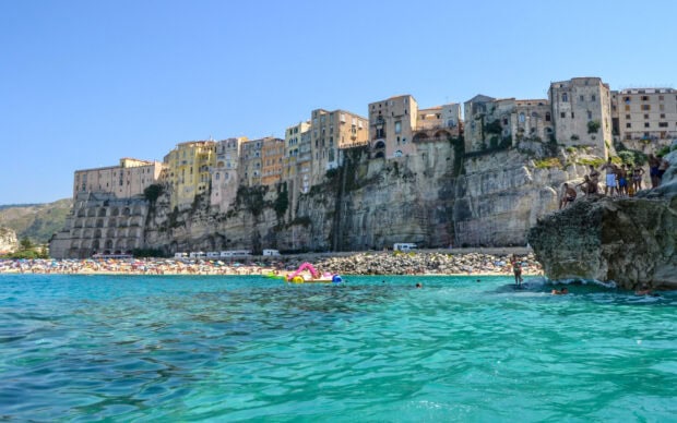 Colorful buildings on cliffs in Tropea with turquoise sea and people enjoying the beach