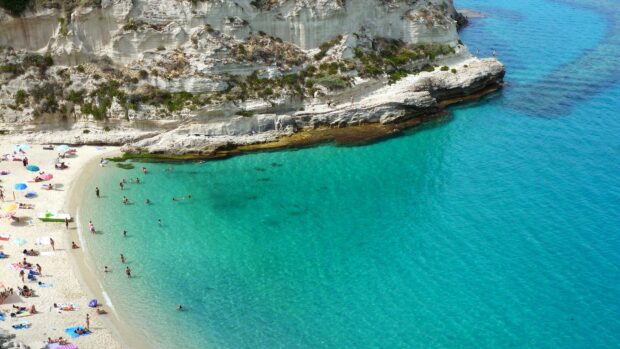 Crystal clear turquoise water at Tropea beach with white cliffs and sunbathers