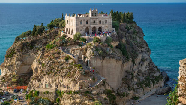 Historic building on rocky cliff in Tropea with sea view and tourists walking
