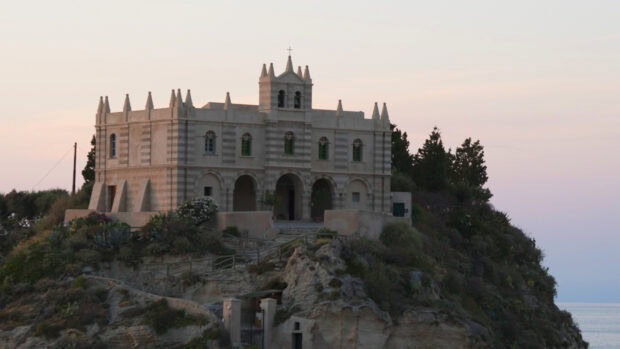 Historic building on Tropea hill at sunset with green windows and Mediterranean plants