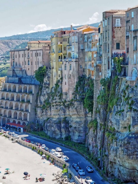 Historic Tropea buildings perched on cliffs above a coastal road in Tropea