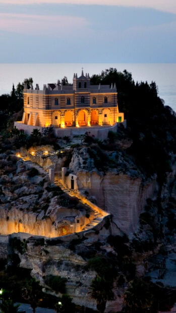 Illuminated cliffside building in Tropea during twilight with scenic coastal view