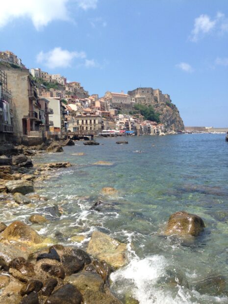 Clear water and rocky coast in Tropea town with historic buildings on the cliff