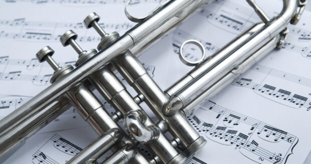 Close up of trumpet valves resting on sheet music with detailed metal textures
