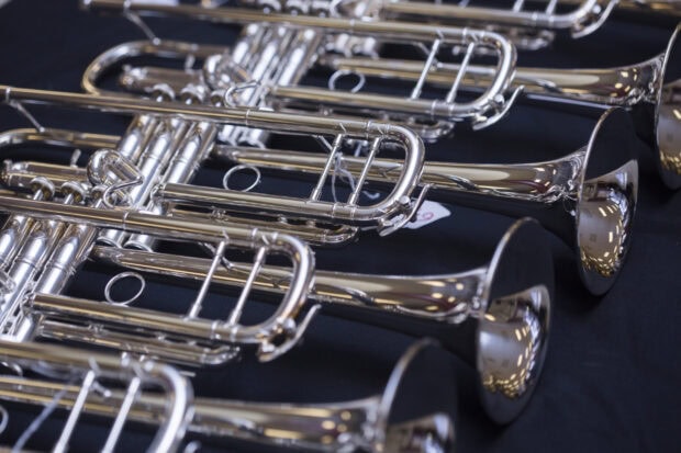 A close up of silver trumpet instruments arranged on a dark surface