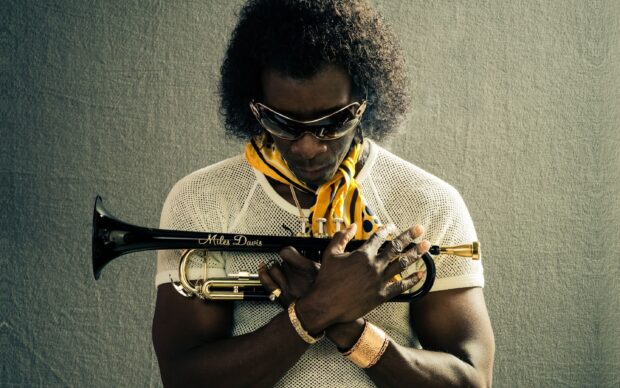 A man holding a trumpet close to his chest with a yellow scarf and sunglasses