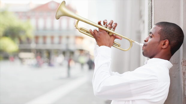 A man playing trumpet outdoors wearing white shirt and concentrating on music