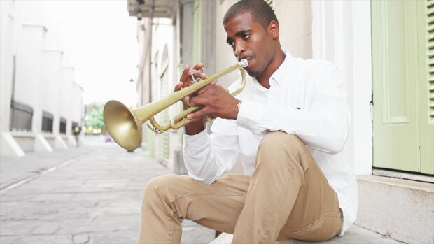 A man sitting on the street playing a trumpet with focus and passion