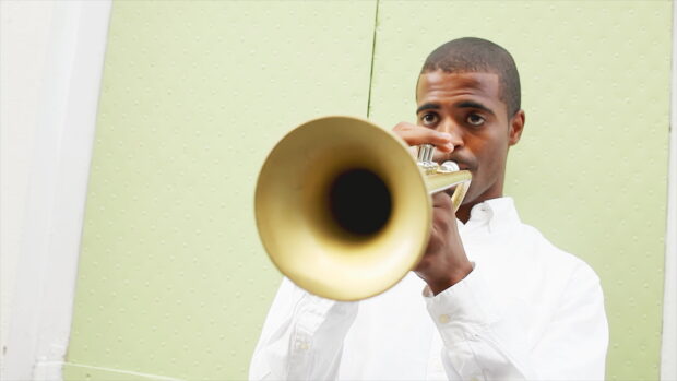A man playing a trumpet in front of a light green wall