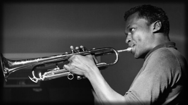 A man playing a trumpet with focused expression in a black and white setting