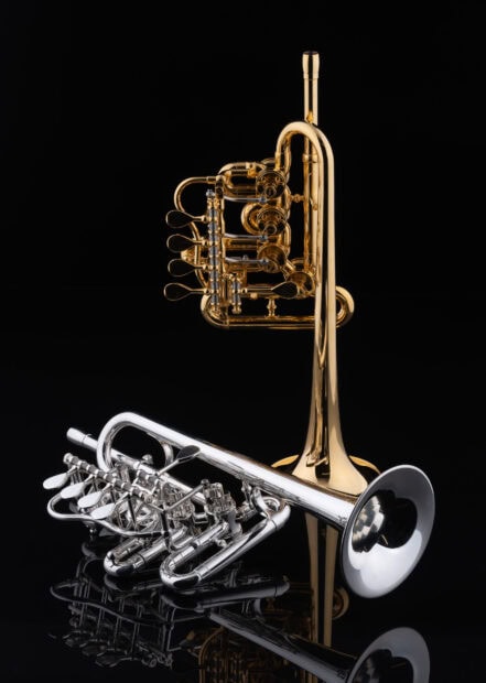 A gold and a silver trumpet placed on a reflective black surface with clear details and shining metal parts