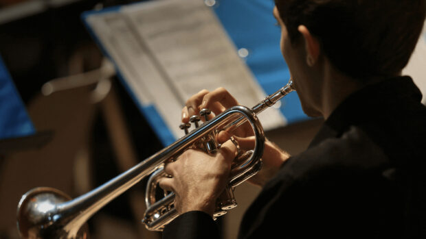 A musician playing a trumpet with sheet music in the background in a concert setting