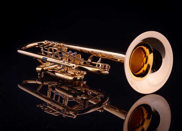 A shiny brass trumpet reflecting on a black surface with detailed valves and tubing