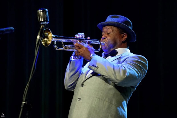 A talented musician playing trumpet passionately on stage in a formal suit and hat