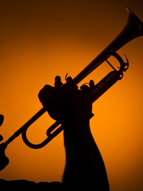 Silhouette of a person playing trumpet with a bright orange background