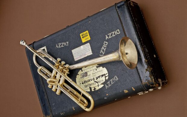 A vintage trumpet resting on an old black suitcase with music stickers