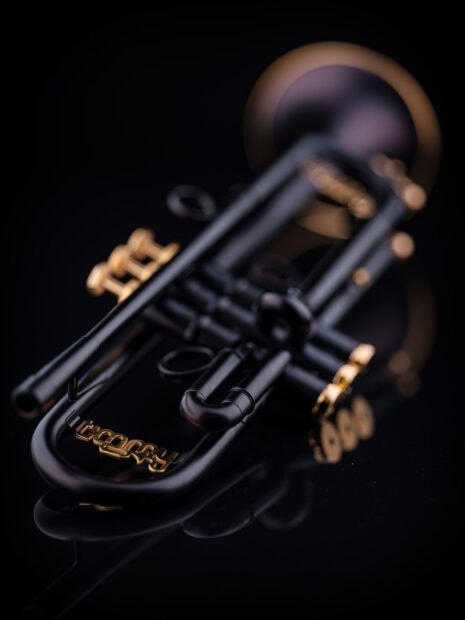 Close up of a black trumpet with gold valves on a dark reflective surface