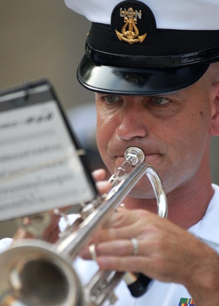 A navy band member playing trumpet with focused expression and sheet music visible