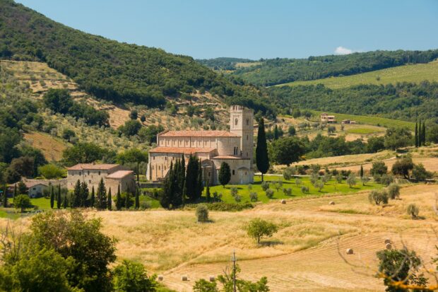 A historic building surrounded by lush green hills and golden fields in Tuscany