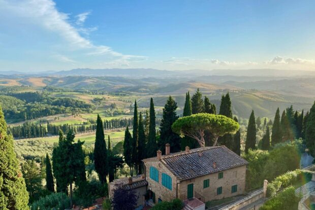 A scenic view of Tuscany with rolling hills and a rustic stone house surrounded by tall cypress trees