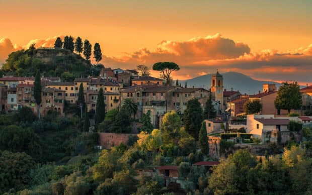 Charming Tuscany village landscape with historic buildings and lush greenery under sunset sky