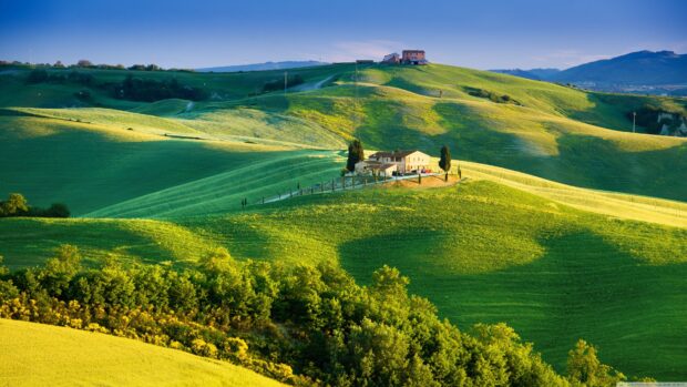 Rolling green hills in Tuscany with a farmhouse on a sunny day