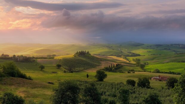 Rolling green hills of Tuscany landscape under a dramatic cloudy sky at sunset