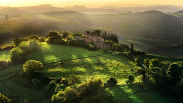Rolling green hills in Tuscany with an old farmhouse surrounded by lush trees and sunlight filtering through the landscape