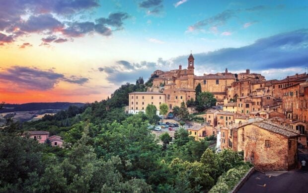 Ancient Tuscany town nestled in lush green hills under a colorful sunset sky