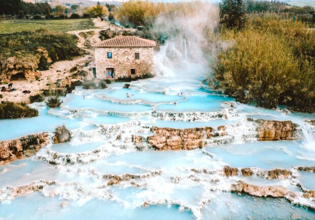 Natural Tuscany pools with a stone house and steam rising in the landscape
