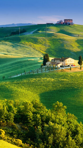 Rolling hills in Tuscany with a rustic farmhouse and lush greenery under a clear sky