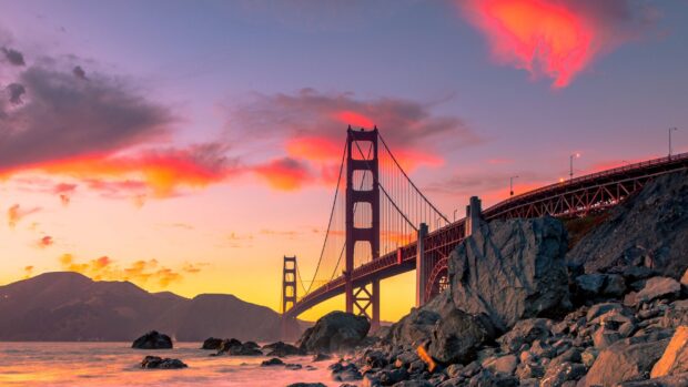 Golden Gate Bridge at sunset with vibrant sky over rocky shoreline in Usa