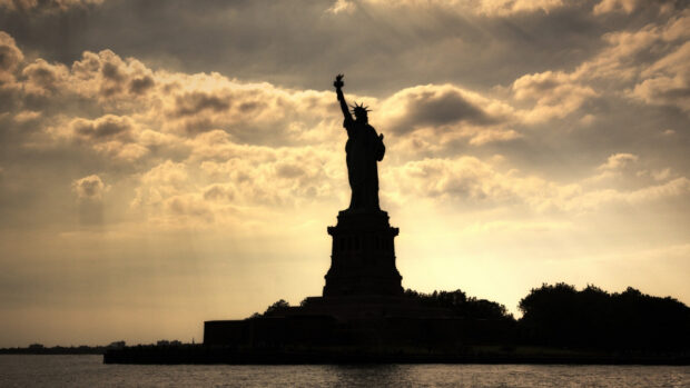 The statue of liberty silhouette stands tall against the cloudy sky at sunset