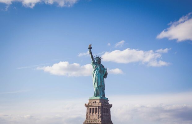 The Statue of Liberty stands tall under a bright blue sky with scattered clouds