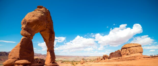 Natural rock formation in Utah under a bright blue sky with scattered clouds