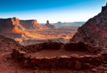 Ancient rock shelter ruins overlook a vast Utah desert landscape with red sandstone formations and clear sky