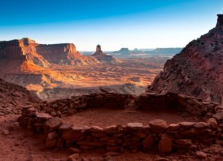 Ancient rock shelter ruins overlook a vast Utah desert landscape with red sandstone formations and clear sky